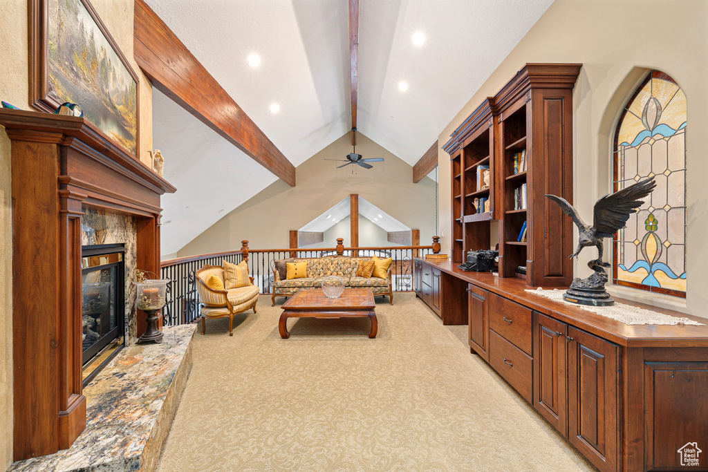 Living room featuring light carpet, lofted ceiling with beams, a premium fireplace, and ceiling fan