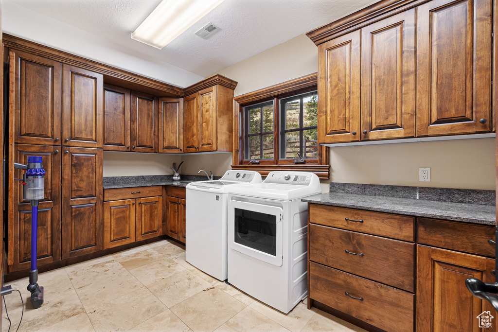 Laundry area featuring washing machine and dryer, a textured ceiling, and cabinets