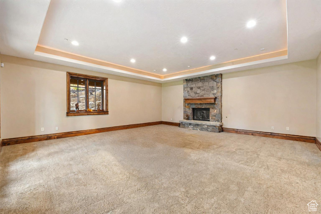 Unfurnished living room featuring carpet floors, a tray ceiling, and a stone fireplace