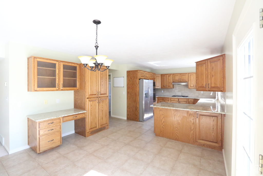 Kitchen featuring stainless steel fridge, pendant lighting, a notable chandelier, decorative backsplash, and kitchen peninsula