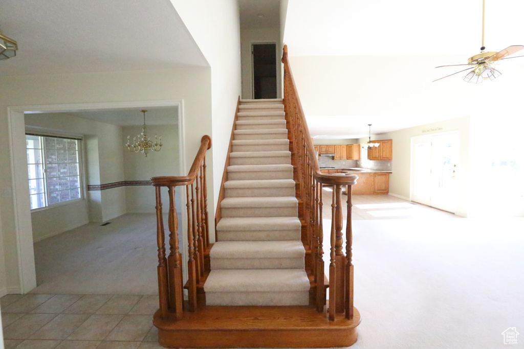 Staircase with ceiling fan with notable chandelier and tile patterned floors