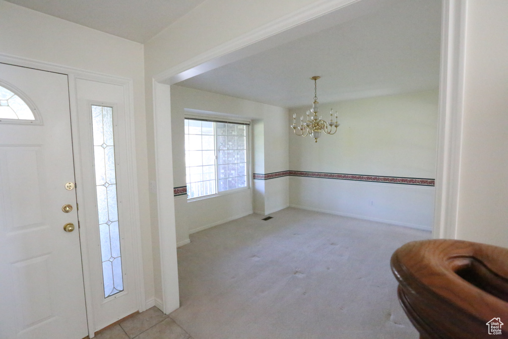 Foyer entrance featuring light colored carpet, a notable chandelier, and a healthy amount of sunlight