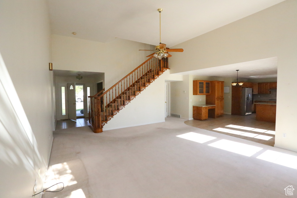 Unfurnished living room featuring ceiling fan, a towering ceiling, and light carpet