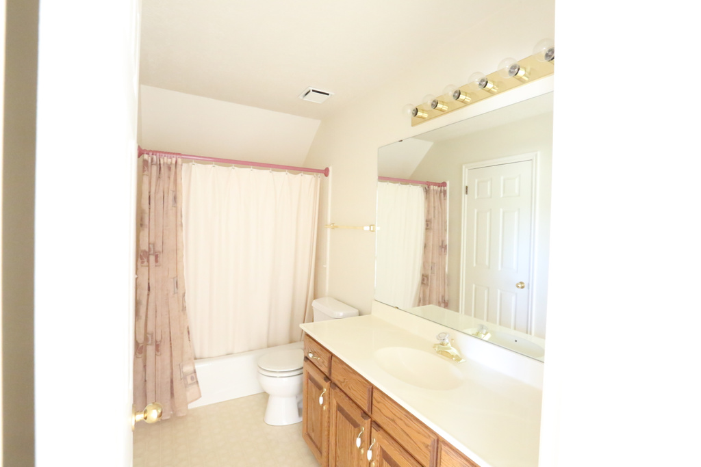 Full bathroom with lofted ceiling, shower / bath combo with shower curtain, vanity, and toilet