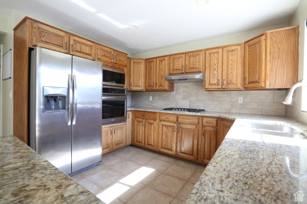 Kitchen with light tile patterned floors, sink, appliances with stainless steel finishes, light stone countertops, and decorative backsplash