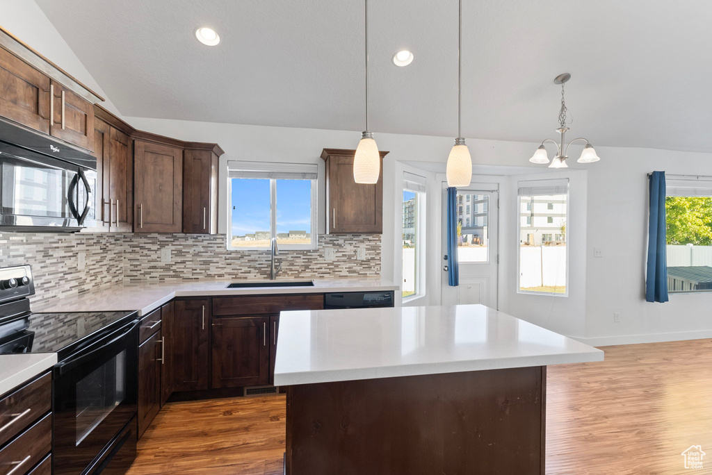 Kitchen with lofted ceiling, black appliances, a kitchen island, sink, and hanging light fixtures