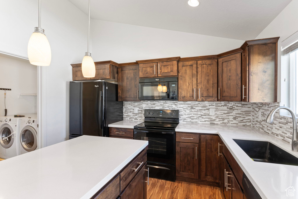 Kitchen with pendant lighting, lofted ceiling, sink, black appliances, and washer and dryer