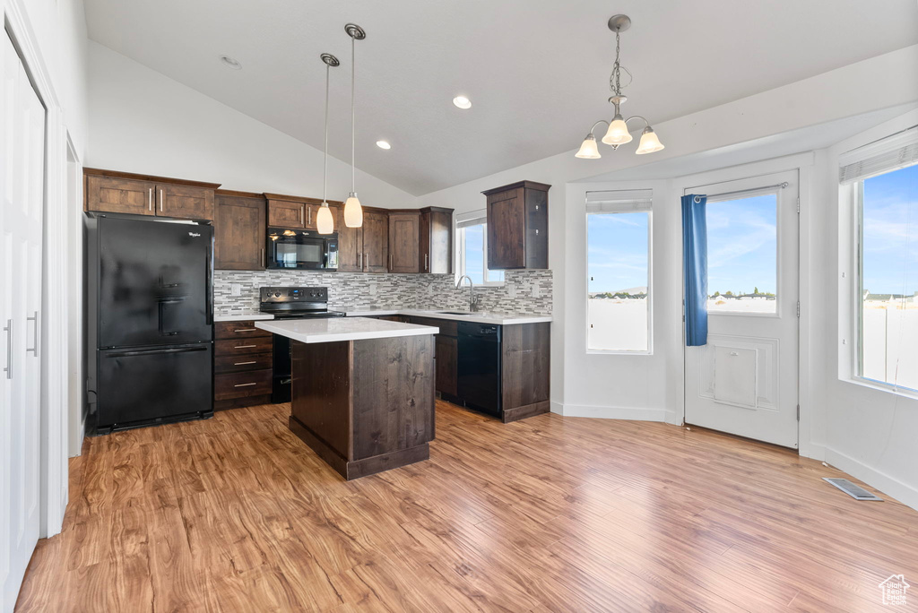 Kitchen featuring light wood-type flooring, pendant lighting, a kitchen island, vaulted ceiling, and black appliances