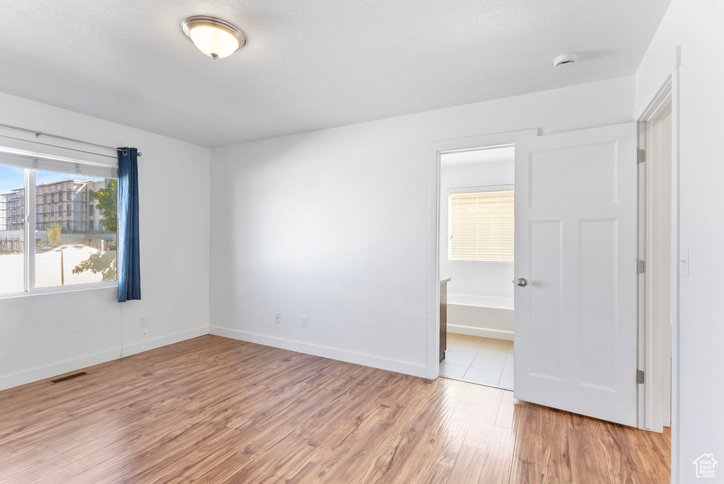 Unfurnished bedroom featuring ensuite bathroom and light hardwood / wood-style floors