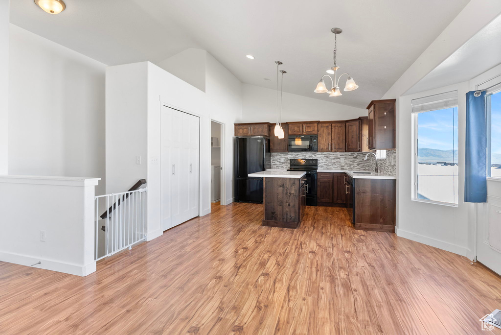 Kitchen with black appliances, a center island, sink, hanging light fixtures, and vaulted ceiling