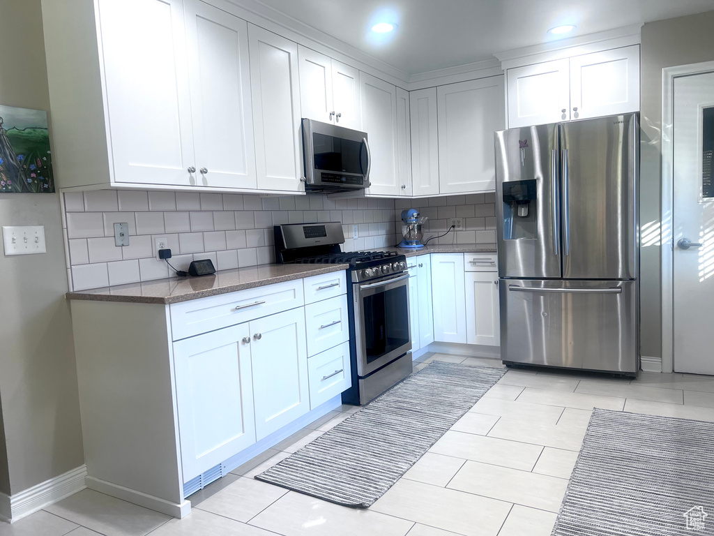 Kitchen featuring white cabinets, appliances with stainless steel finishes, dark stone counters, and decorative backsplash