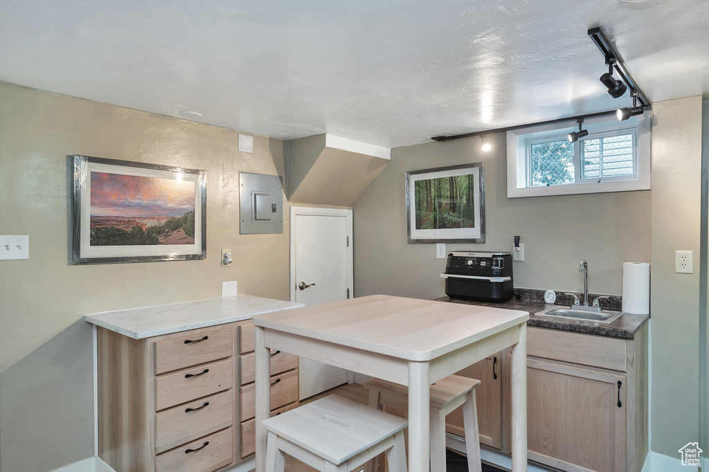 Kitchen featuring light brown cabinets, sink, electric panel, dark stone counters, and track lighting