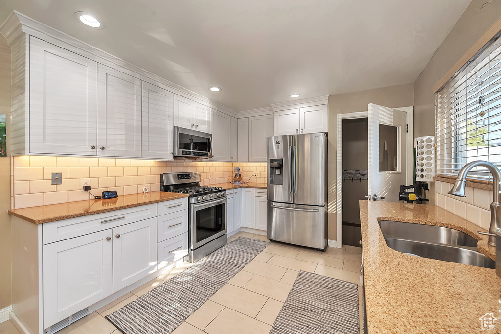 Kitchen featuring white cabinets, appliances with stainless steel finishes, sink, and light stone counters