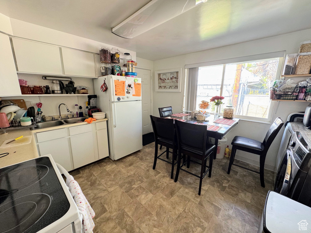 Kitchen featuring white refrigerator, sink, range, and white cabinetry