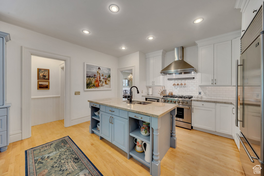 Kitchen with wall chimney exhaust hood, white cabinets, a kitchen island with sink, and premium appliances