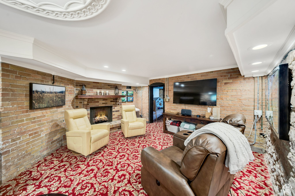 Living room featuring crown molding, brick wall, carpet floors, and a fireplace