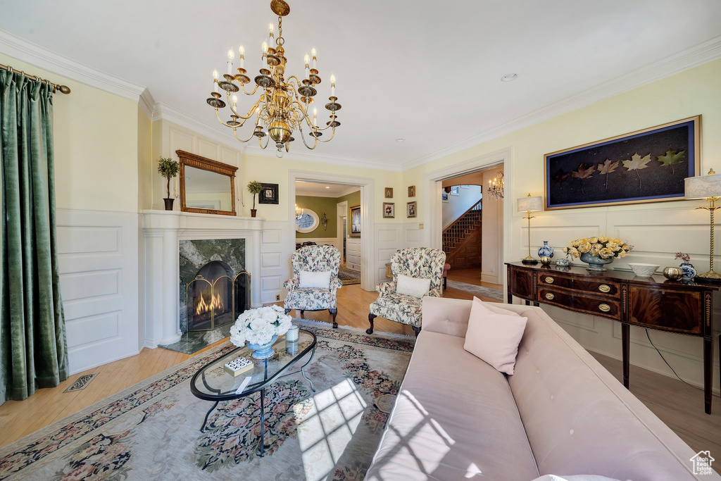 Living room featuring a premium fireplace, light hardwood / wood-style flooring, ornamental molding, and a notable chandelier