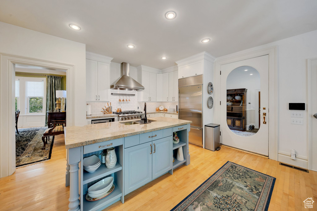 Kitchen featuring light hardwood / wood-style floors, wall chimney exhaust hood, white cabinets, and built in fridge