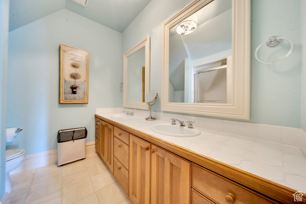 Bathroom featuring toilet, tile patterned flooring, vaulted ceiling, vanity, and walk in shower