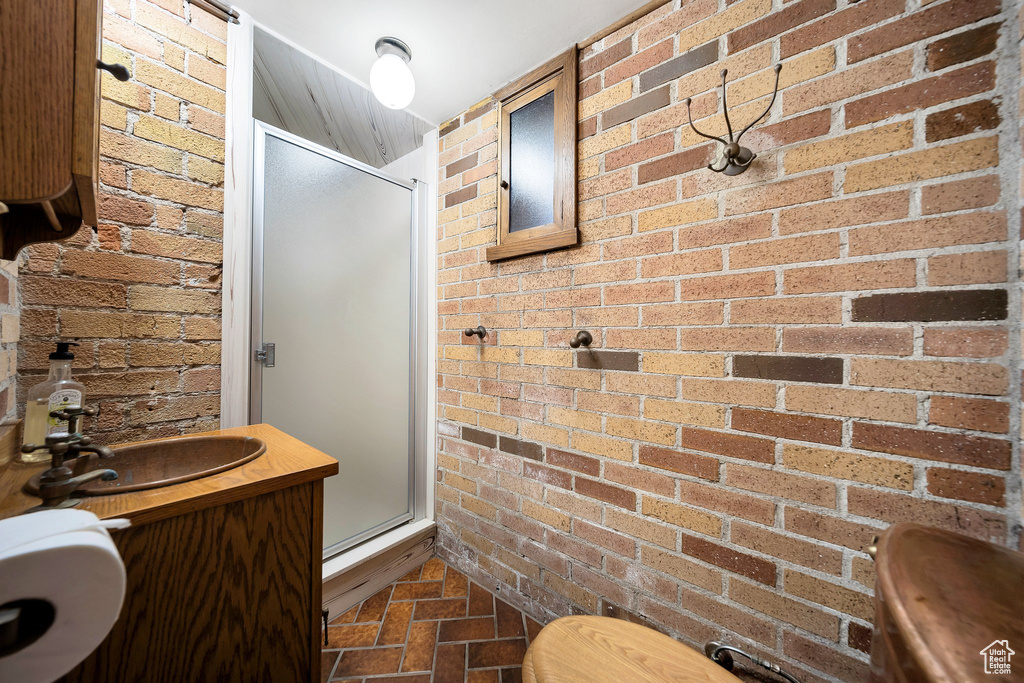 Bathroom featuring a shower with door, brick wall, sink, and toilet