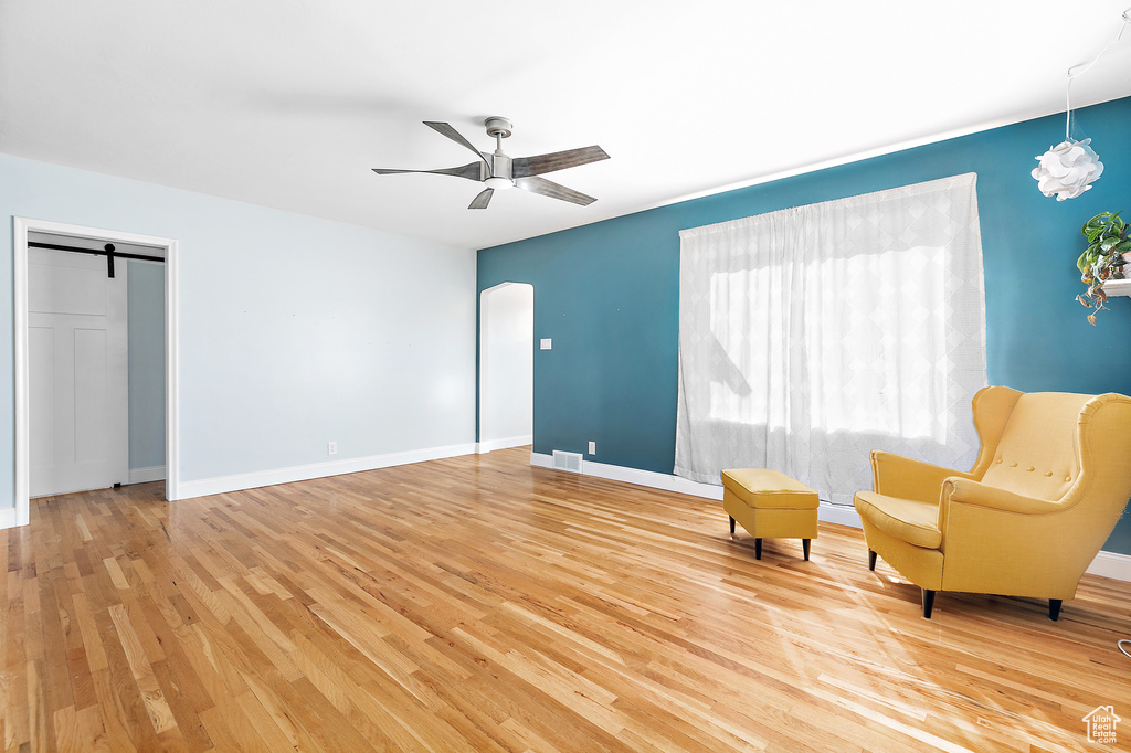 Unfurnished room with a barn door, hardwood / wood-style flooring, and ceiling fan