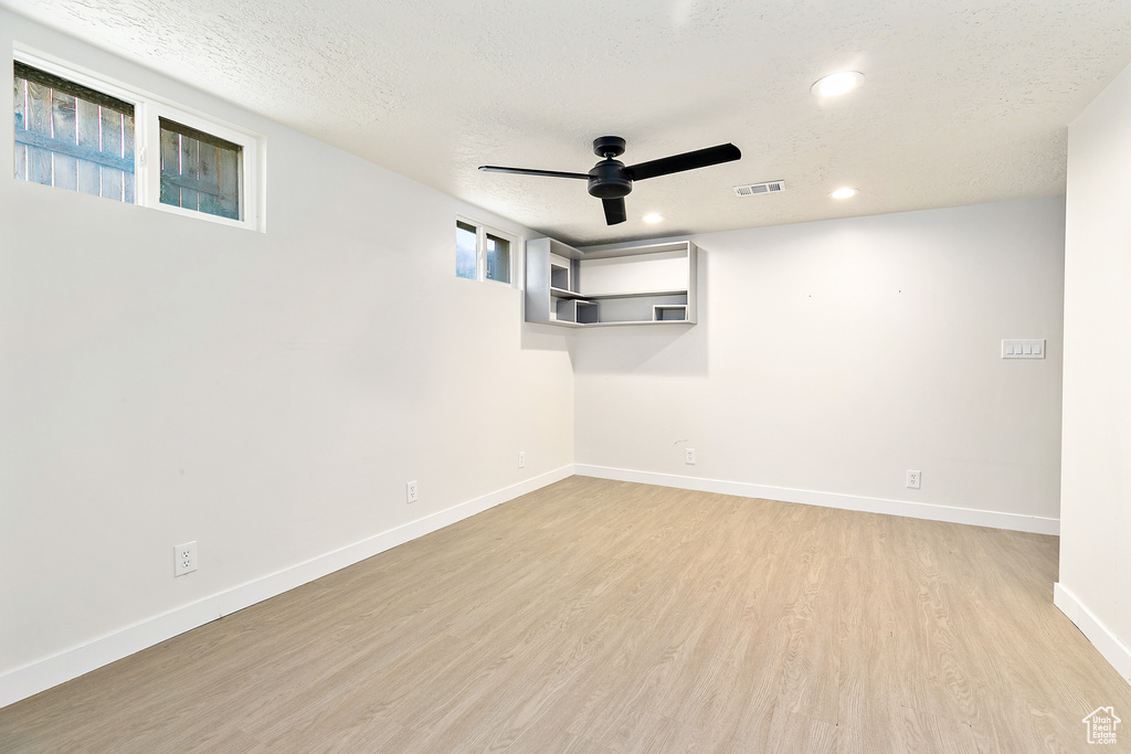 Basement with a textured ceiling, ceiling fan, and light hardwood / wood-style flooring