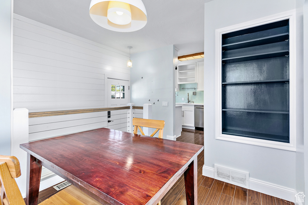 Dining space with sink, wood walls, and dark wood-type flooring