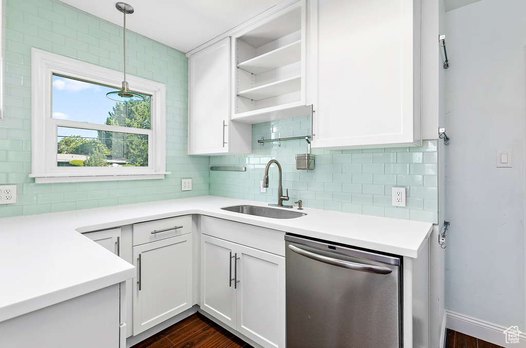 Kitchen with stainless steel dishwasher, white cabinets, dark wood-type flooring, sink, and hanging light fixtures