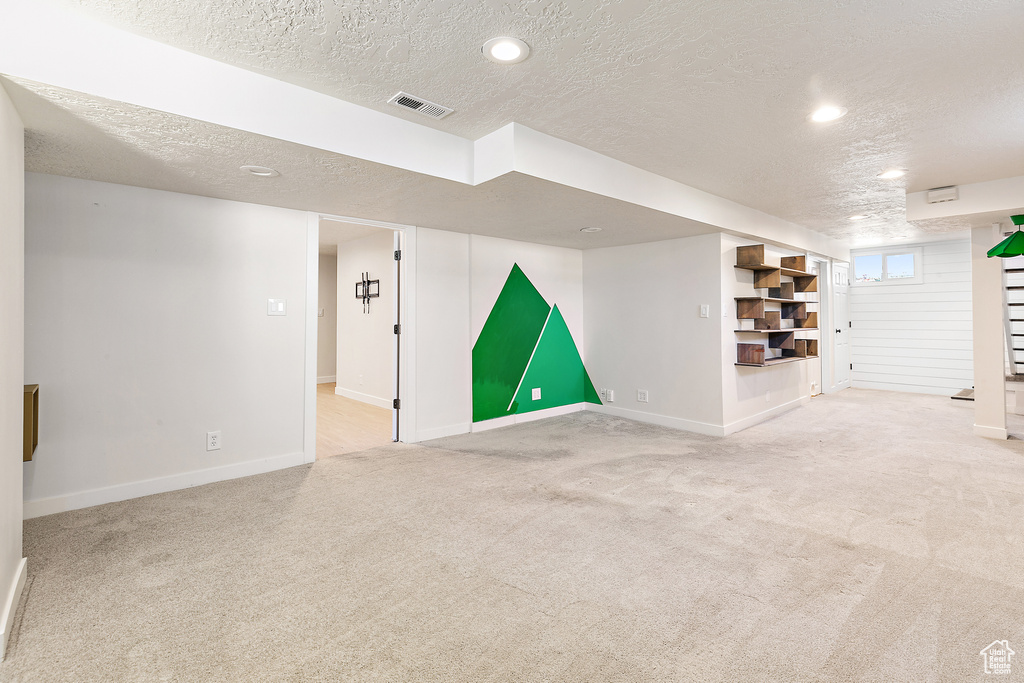 Basement featuring light carpet and a textured ceiling