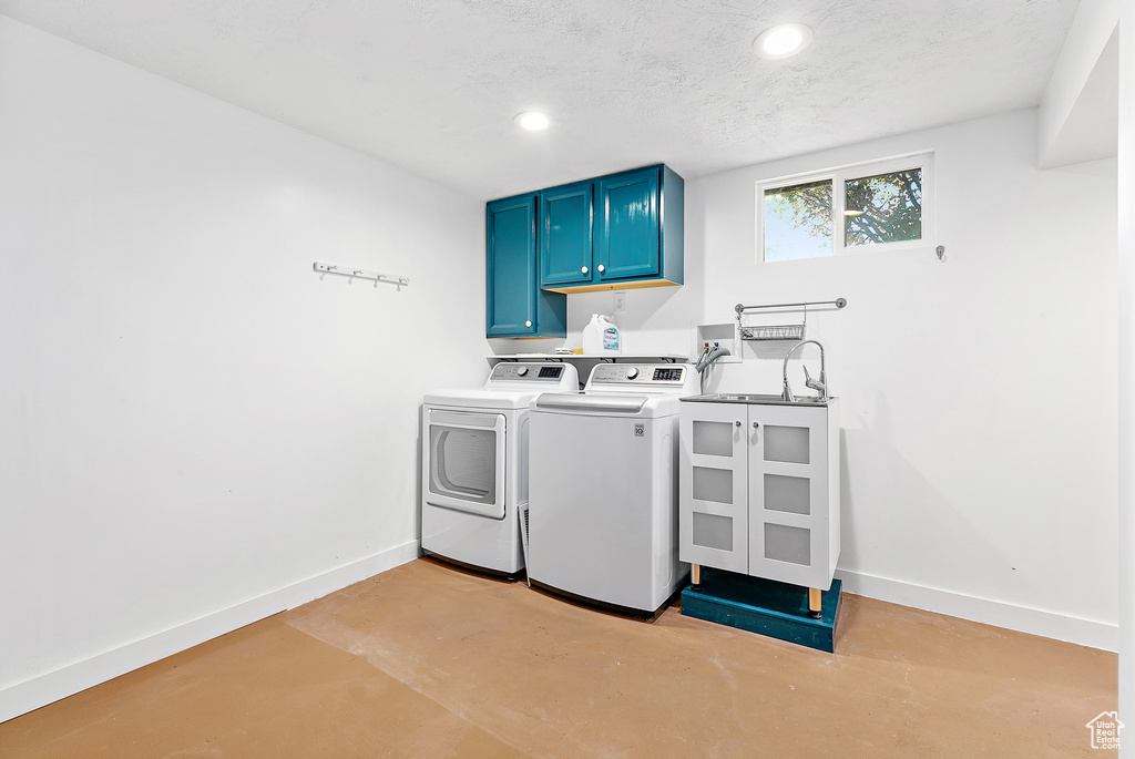 Clothes washing area featuring a textured ceiling, washer and dryer, and cabinets