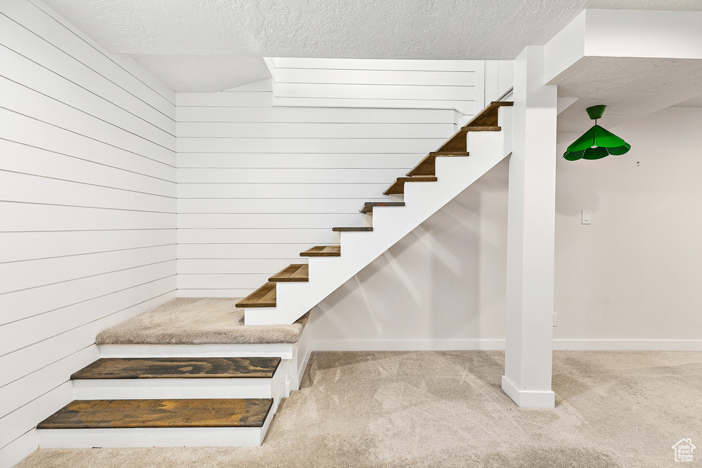 Stairs featuring carpet floors, a textured ceiling, and wood walls