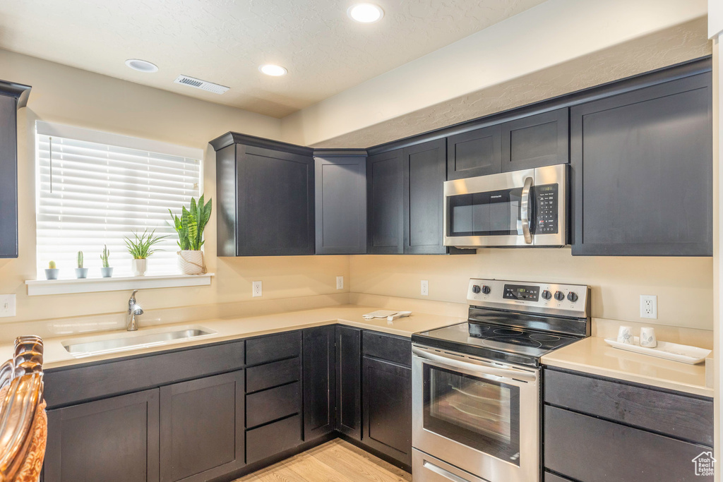 Kitchen featuring appliances with stainless steel finishes, sink, light wood-type flooring, and a textured ceiling