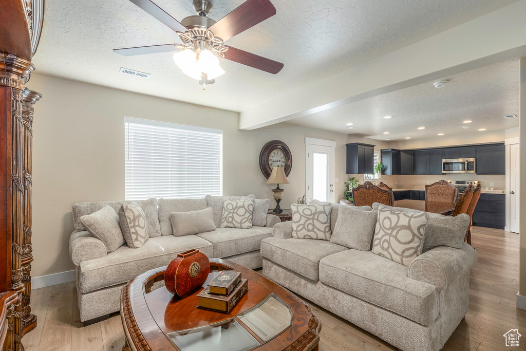 Living room featuring ceiling fan, beam ceiling, light hardwood / wood-style flooring, and a textured ceiling