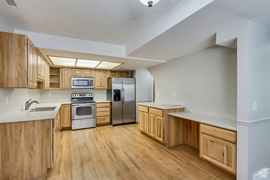 Kitchen with light hardwood / wood-style flooring, sink, kitchen peninsula, appliances with stainless steel finishes, and a textured ceiling