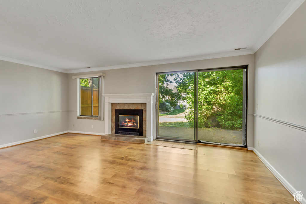 Unfurnished living room featuring a textured ceiling, light wood-type flooring, ornamental molding, and a tile fireplace