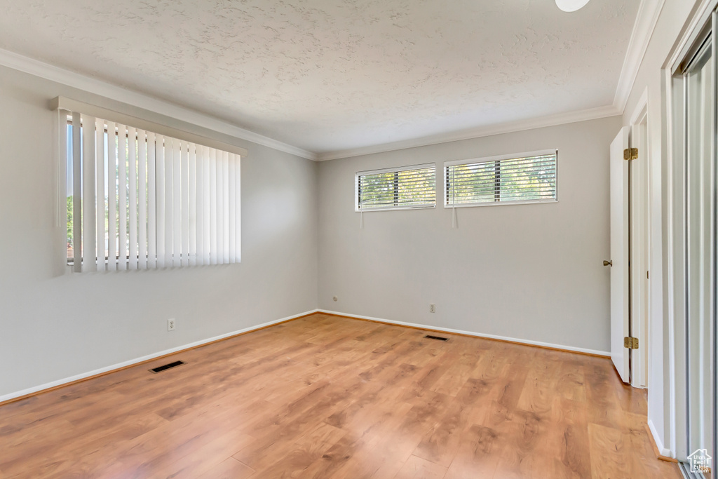 Empty room with crown molding, light hardwood / wood-style flooring, and a textured ceiling