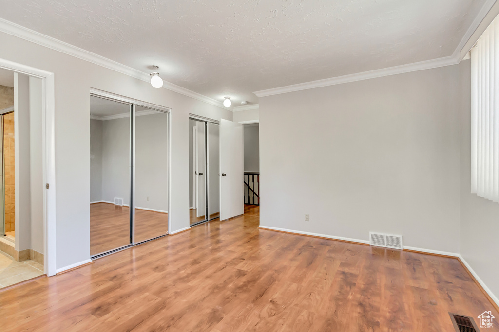 Unfurnished bedroom with connected bathroom, ornamental molding, wood-type flooring, a textured ceiling, and two closets