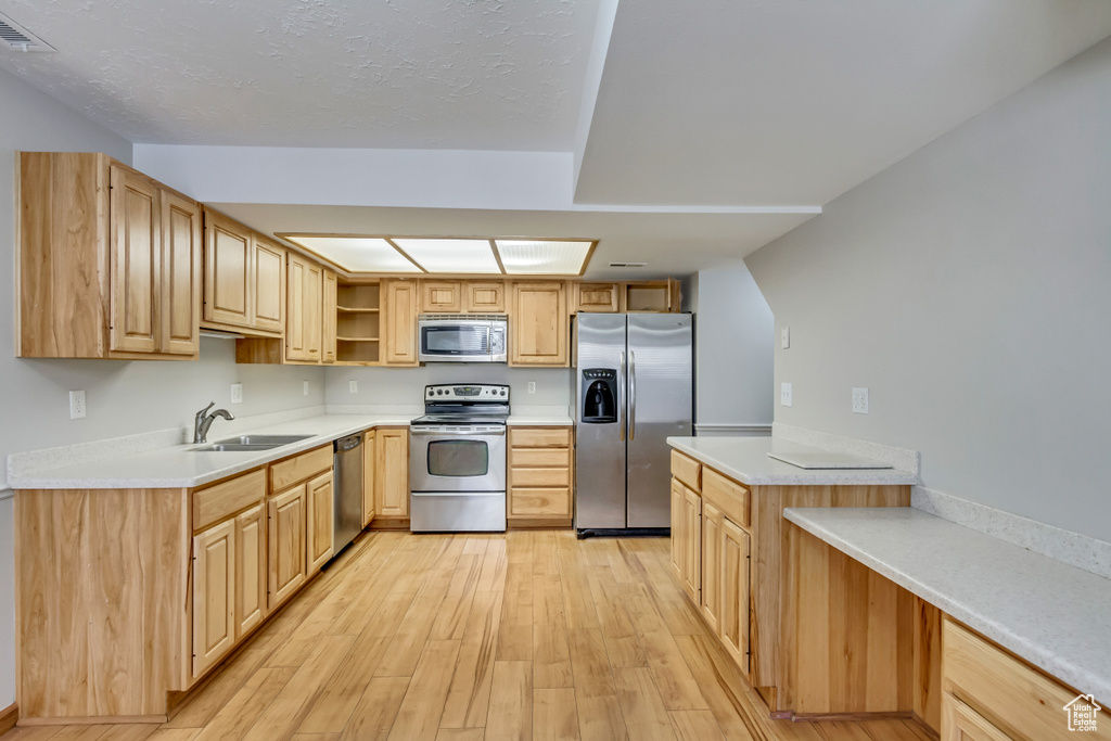 Kitchen with light brown cabinetry, light hardwood / wood-style floors, sink, and stainless steel appliances