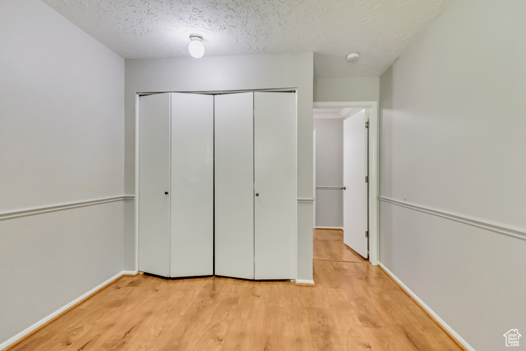 Unfurnished bedroom featuring a textured ceiling, a closet, and light hardwood / wood-style floors