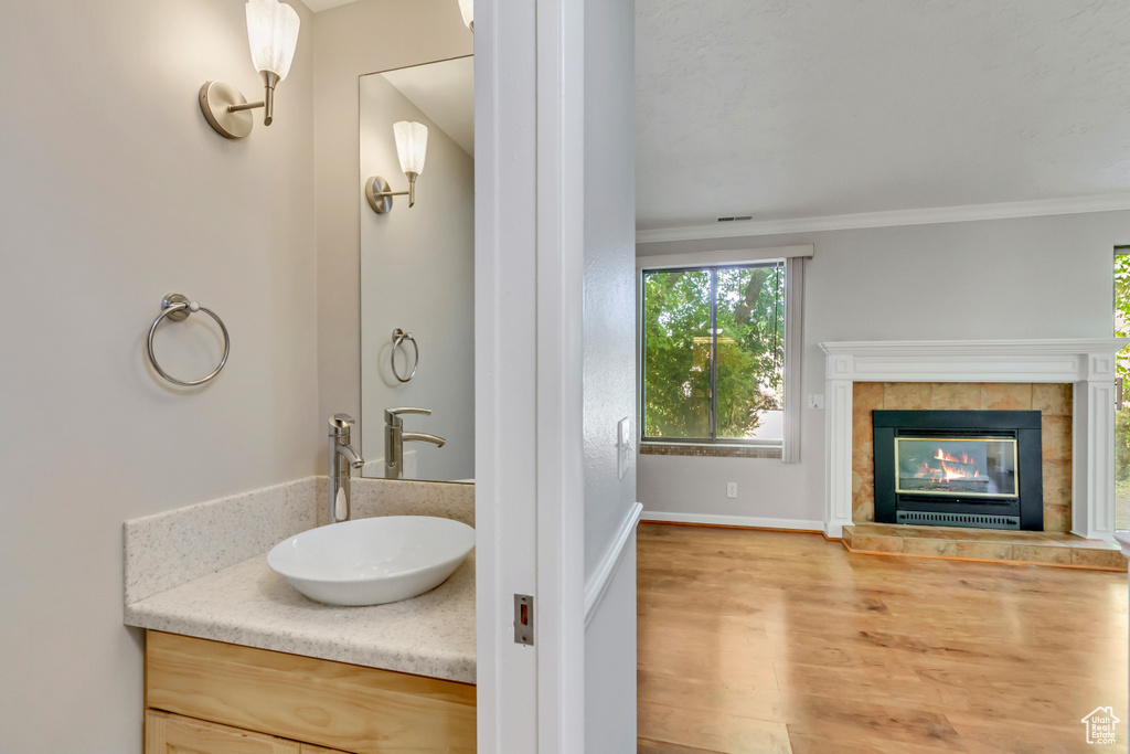 Bathroom with vanity, crown molding, a tiled fireplace, and hardwood / wood-style flooring