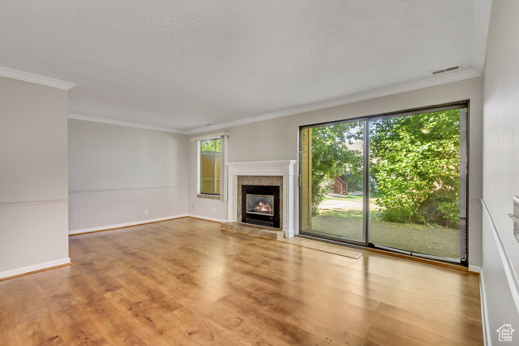 Unfurnished living room featuring light wood-type flooring, crown molding, a tile fireplace, and a textured ceiling