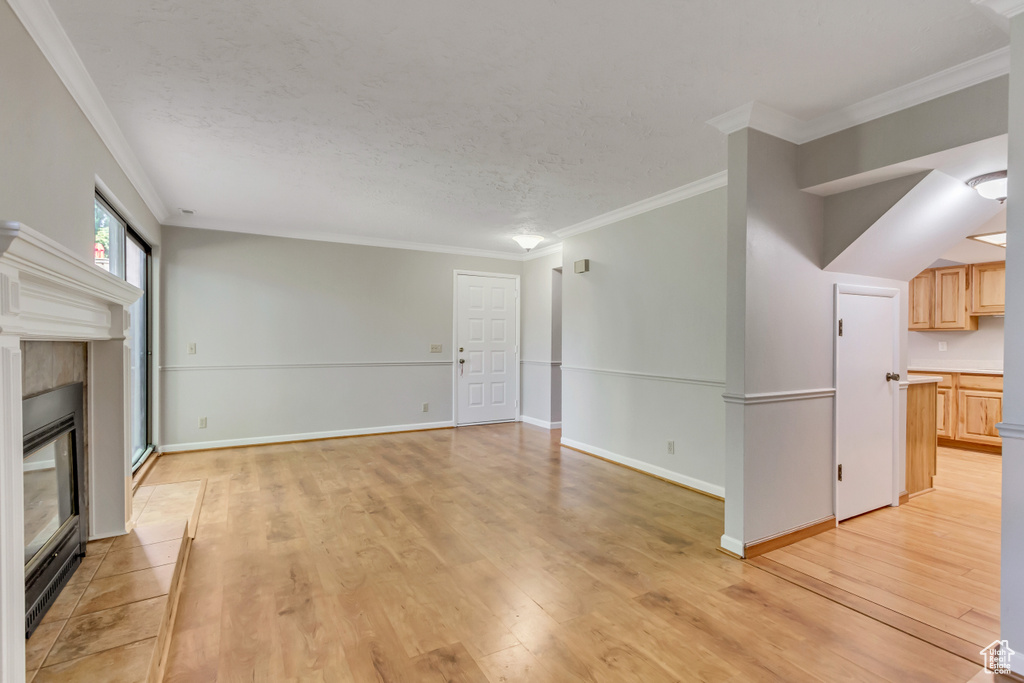 Unfurnished living room featuring crown molding, a tiled fireplace, and light hardwood / wood-style floors