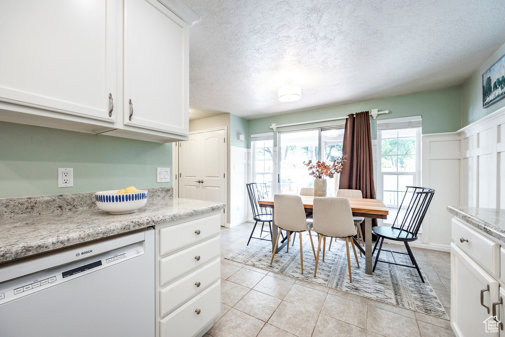 Kitchen with light stone counters, light tile patterned flooring, white cabinetry, white dishwasher, and a textured ceiling