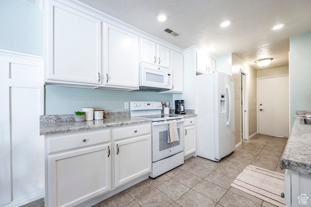 Kitchen with light tile patterned flooring, white appliances, white cabinetry, and a textured ceiling