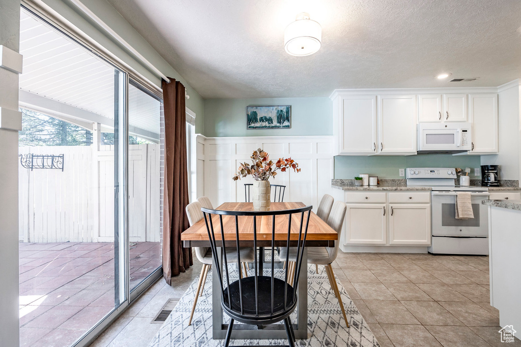 Kitchen featuring light stone countertops, white appliances, white cabinetry, light tile patterned floors, and a textured ceiling