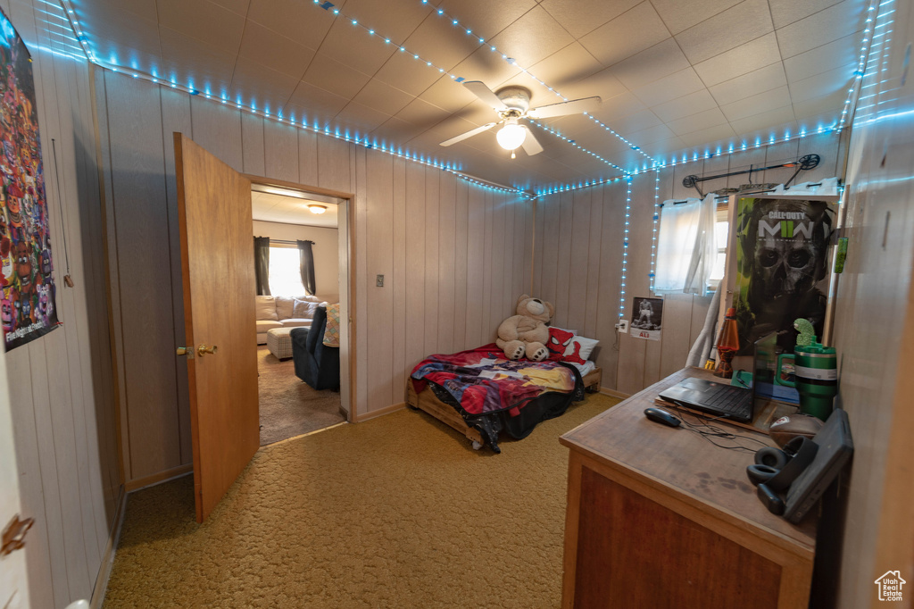 Carpeted bedroom featuring ceiling fan, multiple windows, and wooden walls