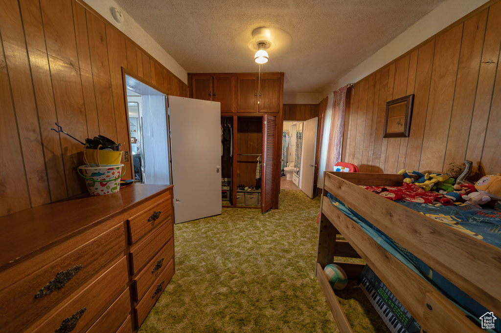 Bedroom featuring light carpet, wood walls, and a textured ceiling