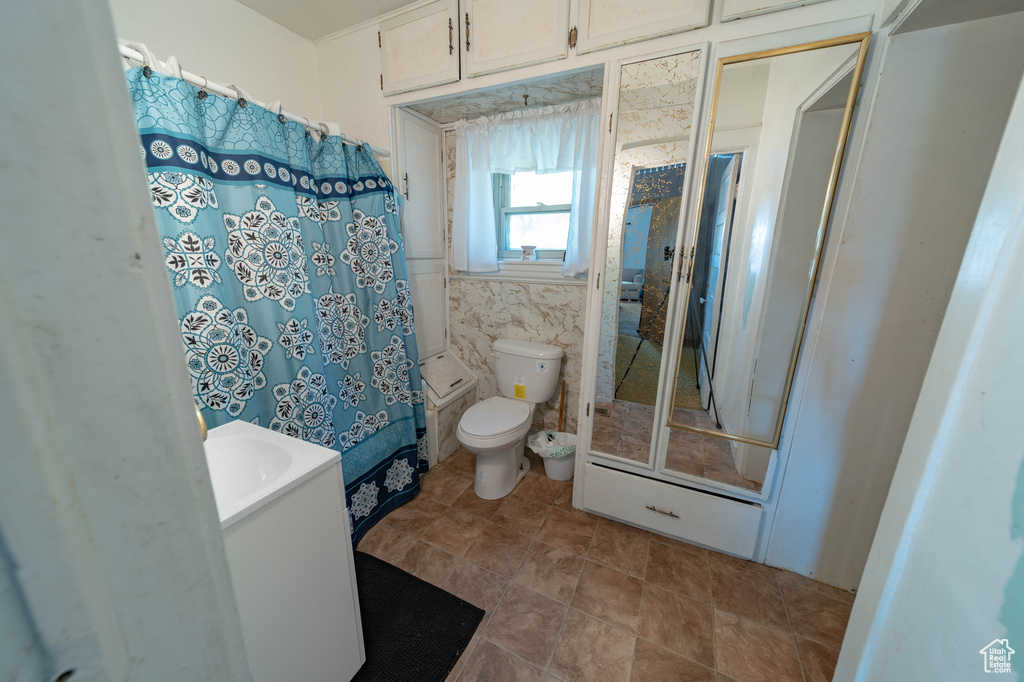 Bathroom featuring curtained shower, tile walls, vanity, and toilet