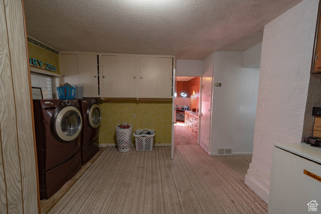 Laundry room featuring washer and clothes dryer, cabinets, a textured ceiling, and light colored carpet