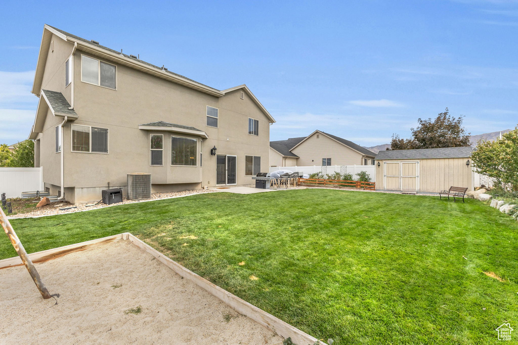 Rear view of house with central AC, a storage unit, a lawn, and a patio area